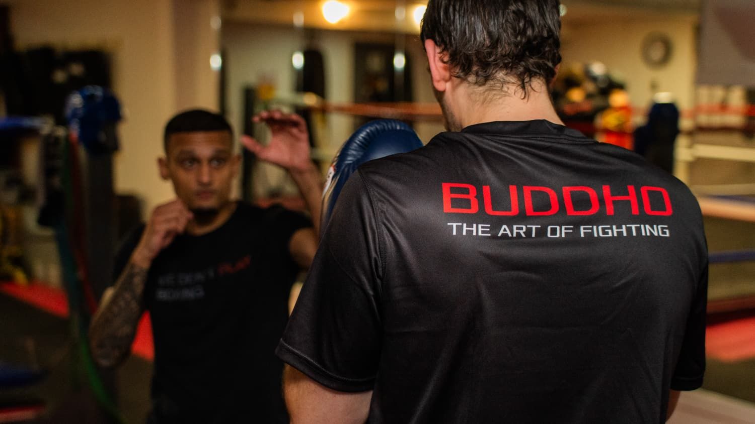 Trainer in Buddho-shirt begeleidt een sporter tijdens een personal training sessie in de vechtsportschool